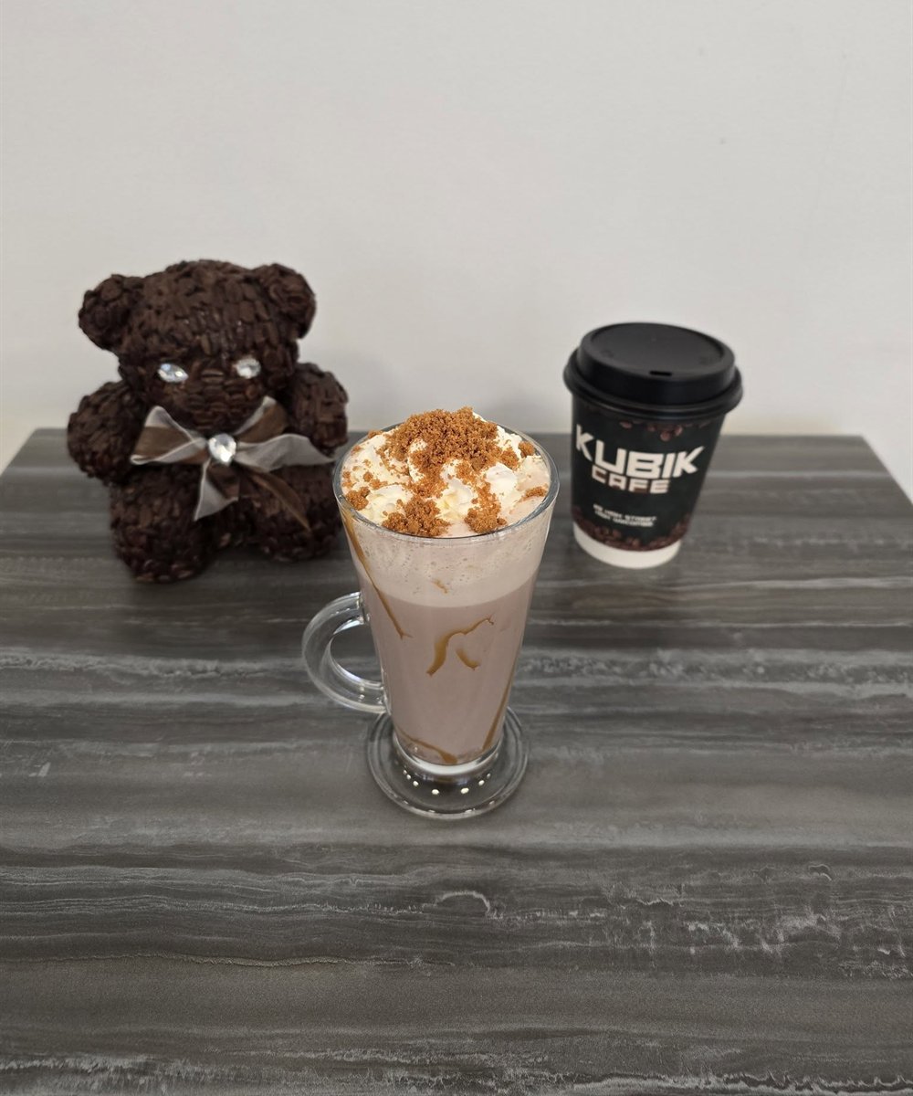 A drink topped with cream next to a Kubik Cafe takeaway cup